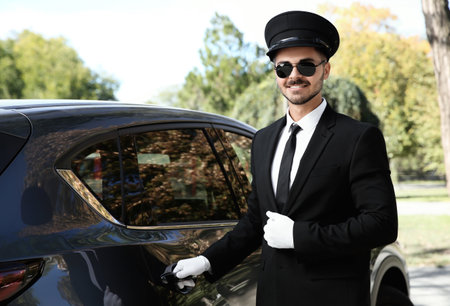 Young handsome driver opening luxury car door. Chauffeur serviceの写真素材