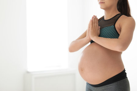 Young pregnant woman in fitness clothes practicing yoga at home, closeup. Space for textの写真素材