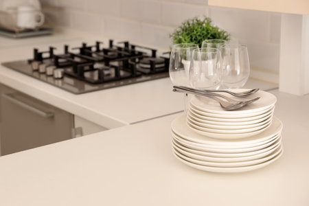 Stack of clean dishes, glasses and cutlery on table in kitchen. Space for text
