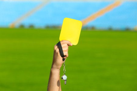 Football referee holding yellow card and whistle at stadium, closeupの写真素材