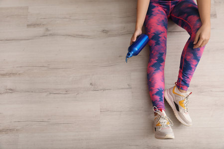Woman in sportswear with bottle of water sitting on floor indoors, top view. Space for textの写真素材