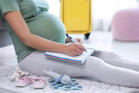 Pregnant woman making list while packing suitcase for maternity hospital at home, closeupの写真素材
