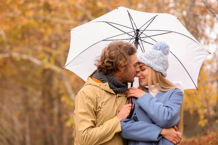 Young romantic couple with umbrella in park on autumn dayの写真素材