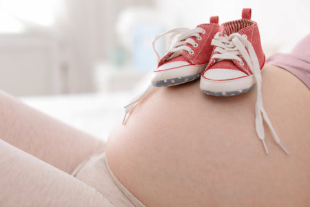 Pregnant woman with baby boots on blurred background, closeup viewの写真素材
