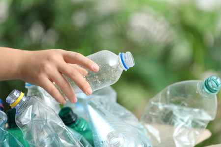 Woman putting used plastic bottle into cardboard box on blurred background, closeup. recycling...