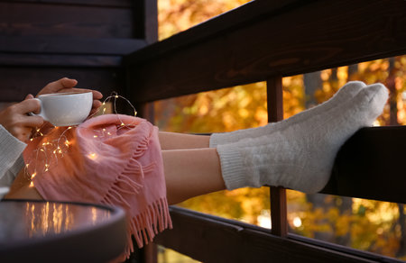 Woman in warm woolen socks with cup of hot cozy drink on balconyの写真素材