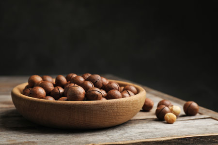 Plate with organic Macadamia nuts on table against dark background. Space for textの写真素材
