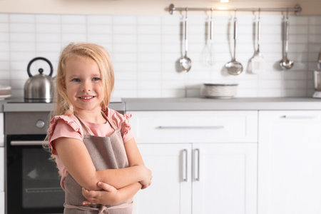 Cute little girl wearing apron near oven in kitchen. Space for textの写真素材