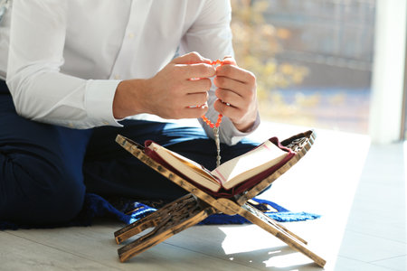 Muslim man with Koran and misbaha praying indoors, closeup