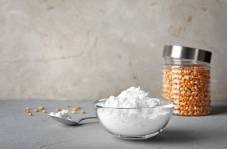 Bowl and spoon with corn starch on gray table. Space for text