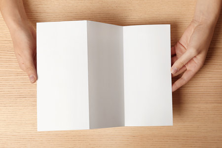 Woman holding blank brochure mock up on wooden table, top viewの写真素材