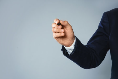 Businessman writing against gray background, closeup view of hand with space for textの写真素材