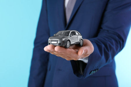 Insurance agent holding toy car on color background, closeupの写真素材