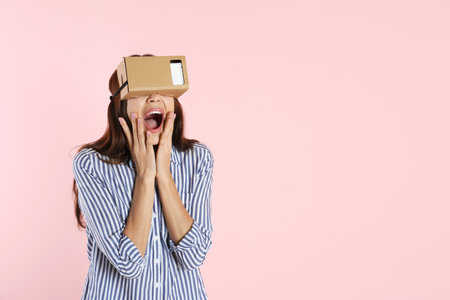 Young woman using cardboard virtual reality headset on color background. Space for textの写真素材
