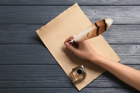 Woman using feather pen to write with ink on parchment at wooden table, top view. Space for textの写真素材