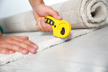 Man cutting new carpet flooring indoors, closeup. Space for textの写真素材