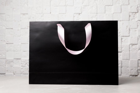 Paper shopping bag with ribbon handles on table near white wall. Mockup for designの写真素材