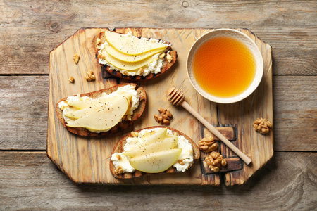 Toasted bread with tasty cream cheese and pear on wooden table, flat layの写真素材