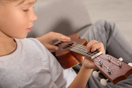 Little boy playing guitar on sofa in room, closeupの写真素材