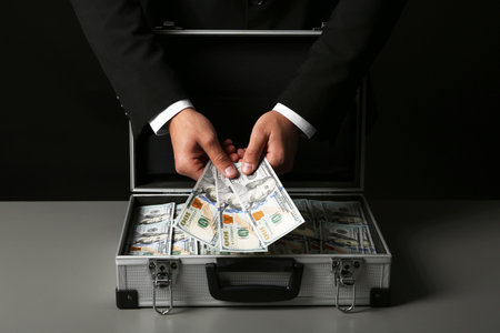 Businessman with suitcase full of money on dark backgroundの写真素材