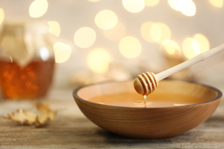 Honey dripping from dipper into bowl on table against blurred lights. Space for textの写真素材