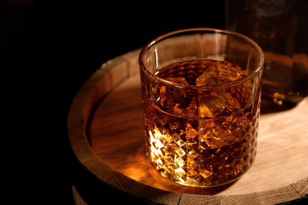 Golden whiskey in glass with ice cubes on wooden barrel. Space for textの写真素材