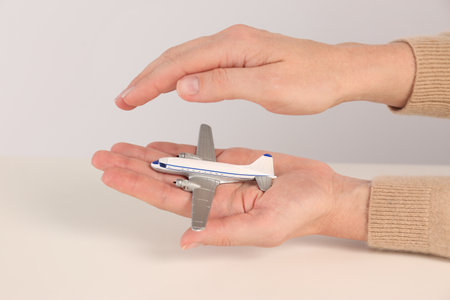 Woman covering toy plane on light background, closeup. travel insurance concept