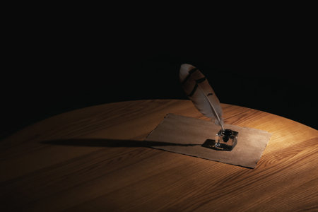Feather pen, inkwell and blank parchment on table in darkness. Space for text