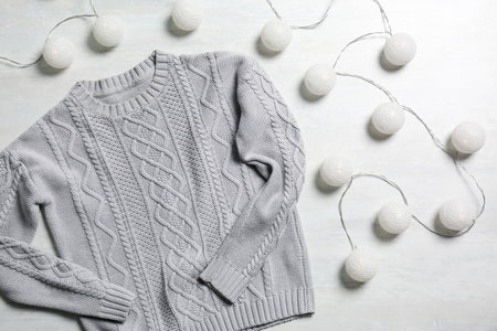 Flat lay composition with warm sweater and fairy lights on light background