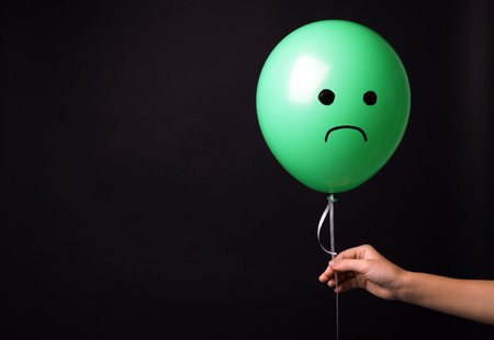 Woman holding balloon with sad face on black background, space for text. Threat of depressionの写真素材