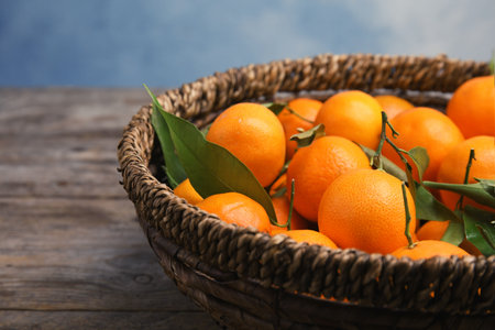 Fresh ripe tangerines in wicker basket on wooden tableの写真素材