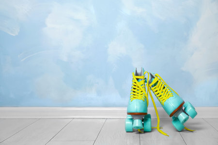 Vintage roller skates on floor near color wall. Space for text