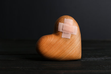 Wooden heart with adhesive plasters in darkness on tableの写真素材