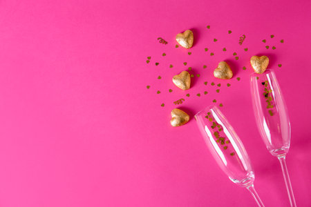 Champagne glasses and heart shaped candies in golden foil on color background, top viewの写真素材