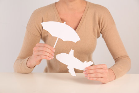 Insurance agent covering paper plane with umbrella cutout at table, closeup. Travel safety conceptの写真素材