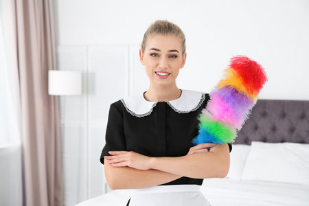 Young chambermaid with dust brush in bedroomの写真素材