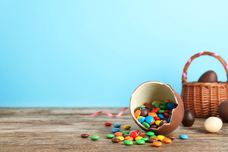 Broken chocolate Easter egg with candies on wooden table. Space for text