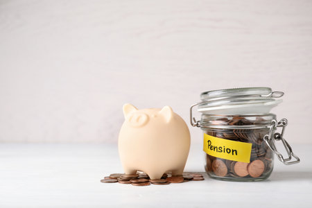 Piggy bank and jar of coins with word PENSION on table. Space for textの写真素材