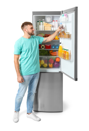 Young man taking bottle of water from refrigerator on white backgroundの写真素材