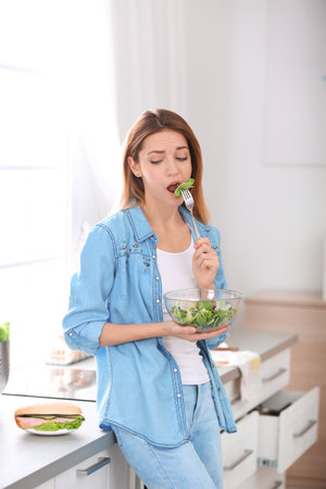 Emotional young woman eating salad instead of sandwich in kitchen. healthy dietの写真素材