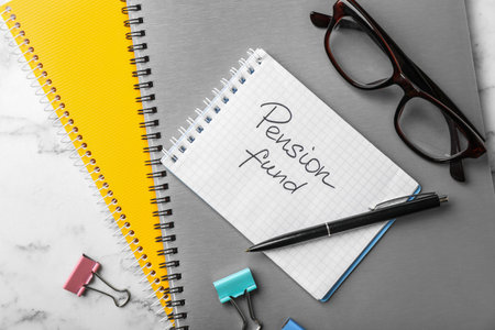Flat lay composition with stationery, glasses and words PENSION FUND written in notebook on tableの写真素材