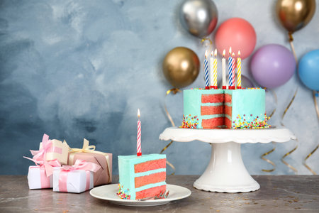 Fresh delicious cake with candles and gifts on table against color background