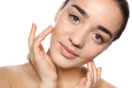 Portrait of young woman with liquid foundation on her face against white backgroundの写真素材