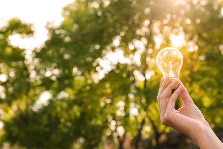 Woman holding lamp bulb outdoors, closeup. Space for text