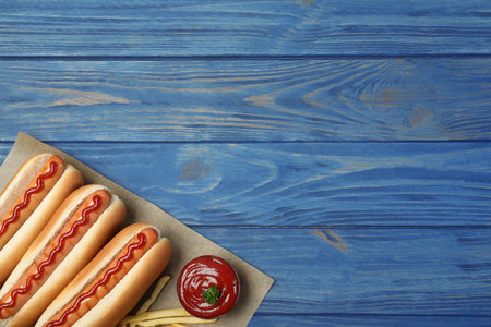 Composition with hot dogs, french fries and sauce on color wooden table, top view. Space for textの写真素材