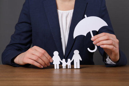 Woman holding cutout paper family and umbrella at table, closeup. life insurance conceptの写真素材