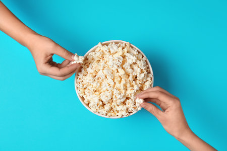 Women eating tasty popcorn from paper bucket on color background, top viewの写真素材