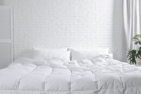 Large comfortable bed with pillows and blanket near white brick wall indoors. Stylish interiorの写真素材
