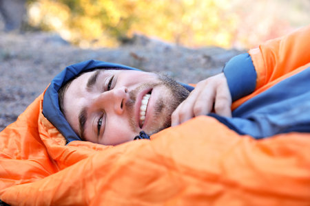 Male camper lying in sleeping bag on ground
