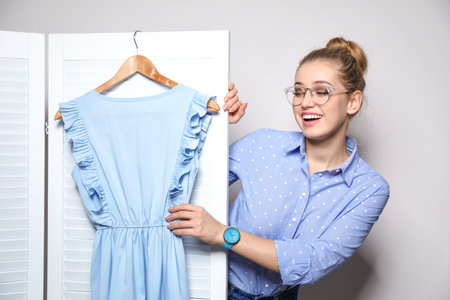 Young woman with clothes on hanger near folding screen against light background. Dressing roomの写真素材